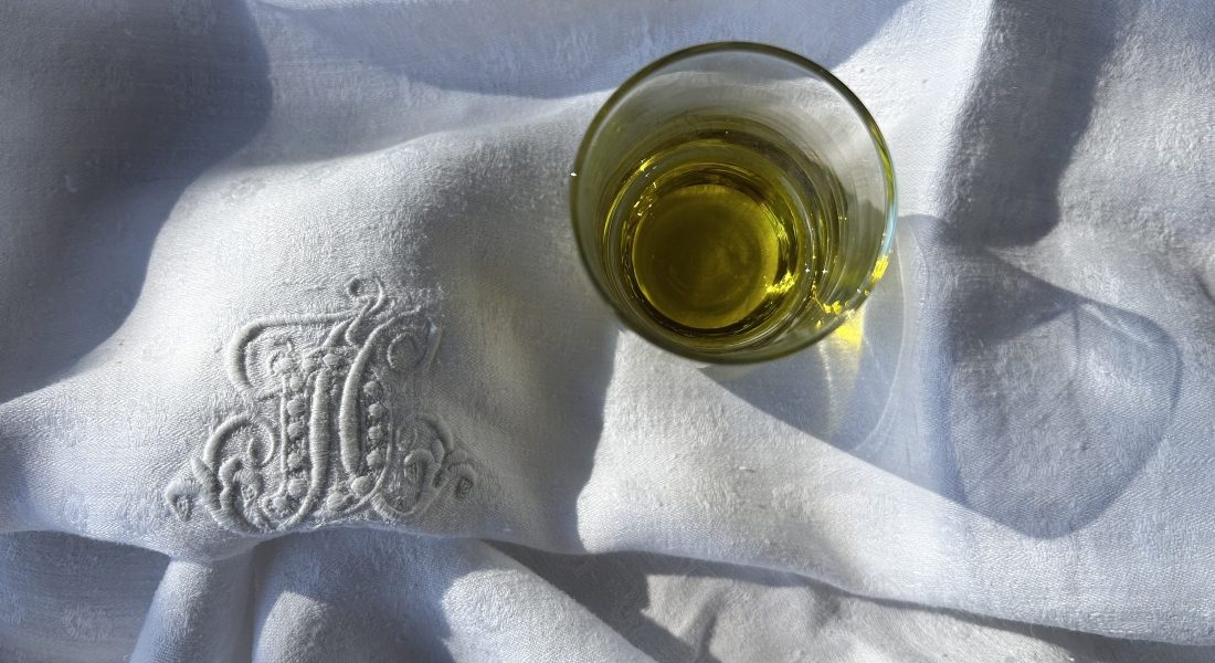 Glass of extra virgin olive oil on white linen cloth in natural sunlight, illustrating olive oil polyphenols and quality