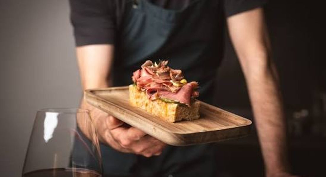 Chef serving a gourmet beef crostini on toasted bread with a glass of red wine