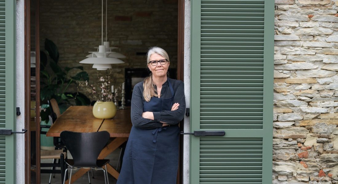 Danish chef and cookbook author Trine Hahnemann standing in the doorway of her home kitchen wearing a blue apron